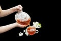 Child`s hands pour tea from jasmine. A glass teapot and a cup of jasmine tea. Isolated on black Royalty Free Stock Photo