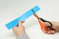 Child`s hands scissor a strip of blue paper on white background