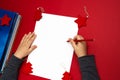 Child`s hands writing a letter to Santa Clause. Blank sheet of white paper on red background with baubles and stack of fairy book Royalty Free Stock Photo