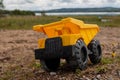 A child`s yellow dump truck abandoned on the ground by a lake Royalty Free Stock Photo