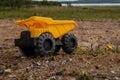 A child`s yellow dump truck abandoned on the ground by a lake, side on view Royalty Free Stock Photo