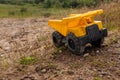 A child`s yellow dump truck abandoned on the ground by a lake, three quarter view Royalty Free Stock Photo