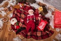 A child in Santa Claus costume rests on a red plaid surrounded by toys