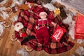 A child in Santa Claus costume rests on a red plaid surrounded by toys.