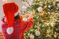 child in santa hat and plaid pajamas decorate the Christmas tree with shiny balls.hands put balls on the branches Royalty Free Stock Photo