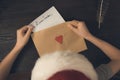 Child in a Santa hat puts a letter for Santa in an envelope. Wooden background. Top view Royalty Free Stock Photo