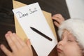 Child in Santa hat is sleeping at the table. Letter for Santa. Wooden background Royalty Free Stock Photo