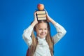 Child schoolgirl smiling and look at camera and put books and appleon head on blue background