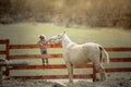 A child a school age boy on a ranch sits on a wooden fence and feeds a pony Royalty Free Stock Photo