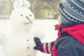 A child sculpts a snowman in the winter on the street, a boy in a red overall