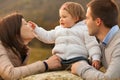 child seated on a hay bale relishes her mother\'s playful faces using a blade of grass