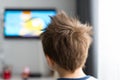 A child of several years standing back in the room looking at the television.