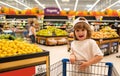 Child with shopping cart full of fresh organic vegetables and fruits standing in grocery department of food store or Royalty Free Stock Photo