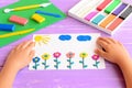 Child shows a card with plasticine flowers, sun and clouds. Supplies for children art crafts on wooden table. Modeling clay craft Royalty Free Stock Photo