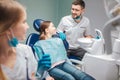 Child sit in denta lchair in room. Male dentist stand beside her and smile. Young woman look at them. She smile too. Royalty Free Stock Photo