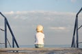 Child sits alone on pier. Sea and sky on background. Back view