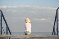 Child sits alone on pier on sea and sky background. Childrens loneliness