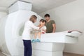 The child sits on a drawer of an MRI machine. Nearby A father and a female doctor are preparing a little girl for Royalty Free Stock Photo