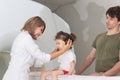 The child sits on a drawer of an MRI machine. Nearby A father and a female doctor are preparing a little girl for Royalty Free Stock Photo