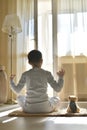 The child sits with his back at home. On the mat with a plush toy dog. Meditation in a yoga pose with hands makes mudra