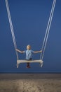 Child sits on rope swing and looks at the sea and magic dark blue sky. Boy swinging during dusk. Back view