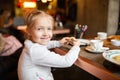 Child sits at a table in a cafe. Happy little girl with blonde hair sitting in restaurant Royalty Free Stock Photo