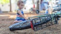 A child sitting in the dirt playing with a bike wheel