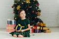 Child sitting on floor near christmas tree, holding gift box and looking away Royalty Free Stock Photo