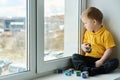 Child sitting at home on windowsill, holding cubes in his hands and looking out window