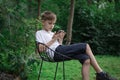 Child sitting in nature and looks at phone. Modern generation gadgets