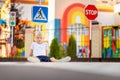 A child is sitting on the road at a pedestrian crossing among road signs, traffic rules for children Royalty Free Stock Photo