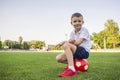 A child is sitting on a soccer ball on the grass of stadium`s field. Training and sports for children concept Royalty Free Stock Photo