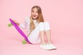 Child skater smiling with longboard. Skateboard kid sit on floor. Small girl smile with skate board on pink background. Childhood