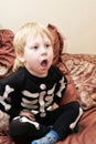 A child in a skeleton costume sits on the couch and coughs or yawns