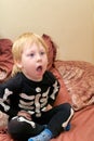 A child in a skeleton costume sits on the couch and coughs or yawns