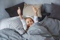 The child sleeps in a gray-colored bed. The girl stretches, spreading her arms in different directions, and shows her thumbs up. Royalty Free Stock Photo