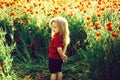 Child or smiling little boy with long blonde hair in red shirt in flower field of poppy with green stem on natural