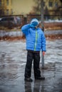 A child in snowboots boots is standing in a puddle of melted snow. Ice on the roads in the city. Not cleaned from snow and ice