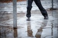 A child in snowboots boots is standing in a puddle of melted snow. Ice on the roads in the city. Not cleaned from snow and ice