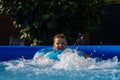 A child splashes in the pool on a summer sunny day. Mila happy boy bathes in the pool on a hot day. The child kicks the Royalty Free Stock Photo