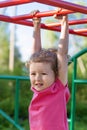 Child and sport. little active emotional girl on playground in park, hanging on horizontal bar, doing sports exercise outdoors.