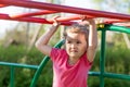 Child and sport. little active emotional pensive girl on playground in park, hanging on horizontal bar,