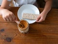 Child eating crispbread with peanut butter on wooden table home kitchen. School girl with bread slice wholegrain snack