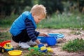 Child squat on the ground playing with sand toys. The child digs the sand into a plastic bucket. Summer outdoor activity for kids Royalty Free Stock Photo