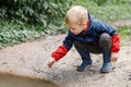 A child squat in a nature explores a dirty swamp, the little one smears his hands and face