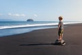 Child stand on big stone on black sand sea beach