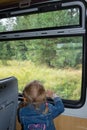 A child stands in the car of a moving train and looks out the window.