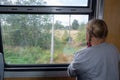 A child stands in the car of a moving train and looks out the window.