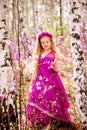 A child stands among the ledum and birch in a pink dress and smiling