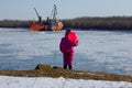 A child stands with a red ball and looks at the ship